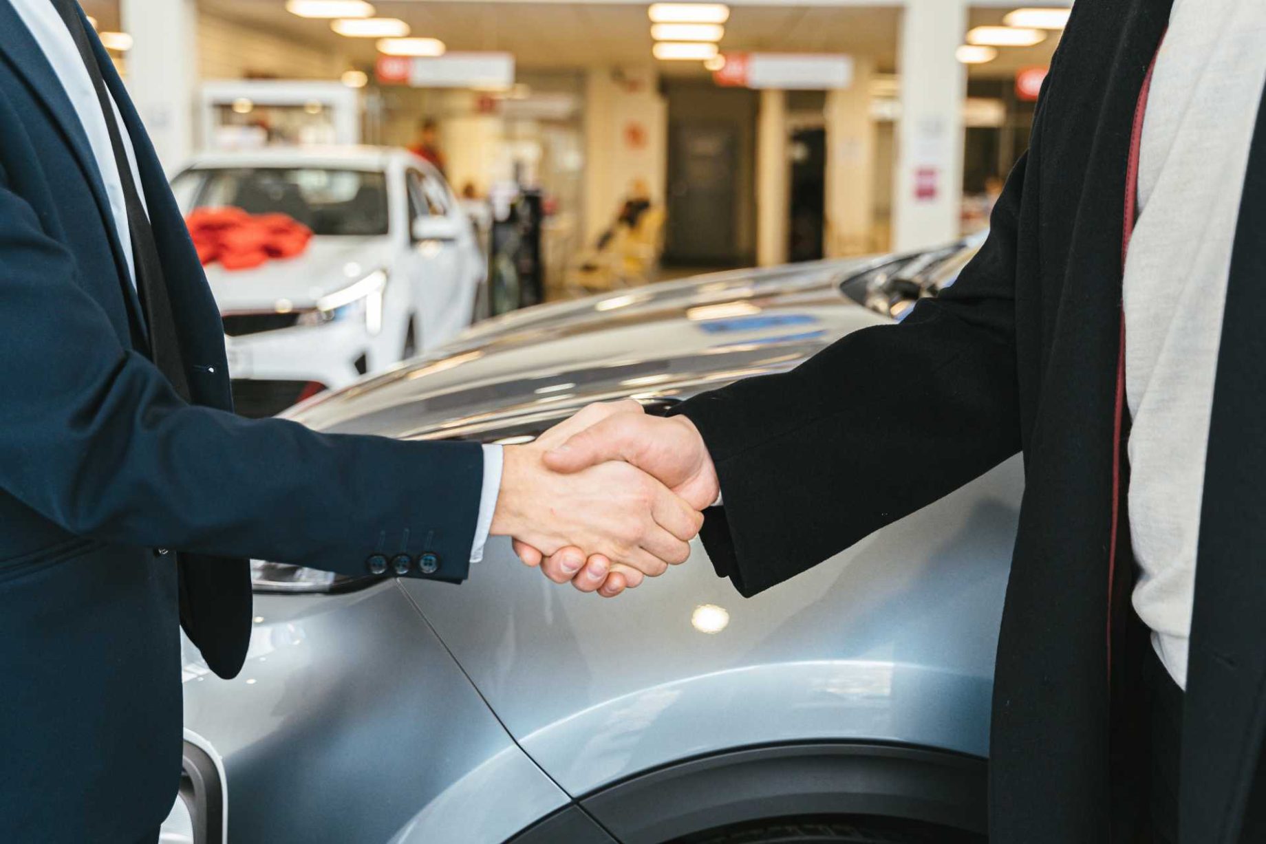 Two people shaking hands in front of a car at a dealership.