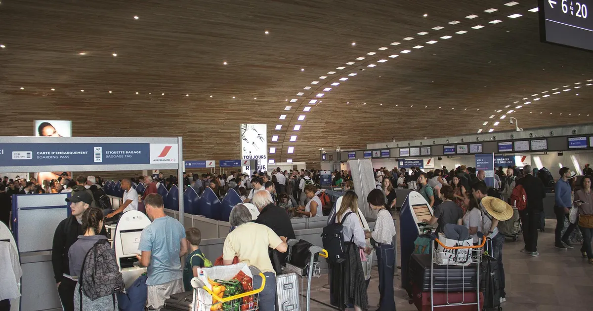 Crowded airport terminal with travellers in line. Indoor setting with modern architecture.