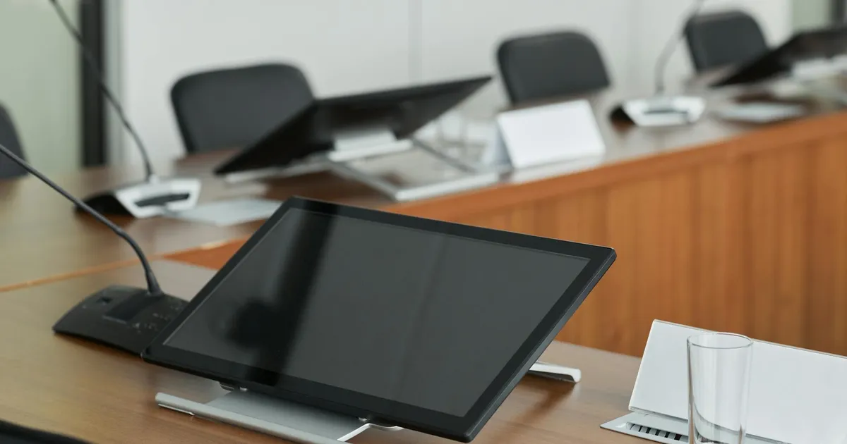 A modern conference room setup featuring digital monitors and microphones on a wooden table.