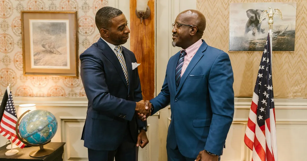 African American men in suits shaking hands in a formal law office setting with USA flags and globe.