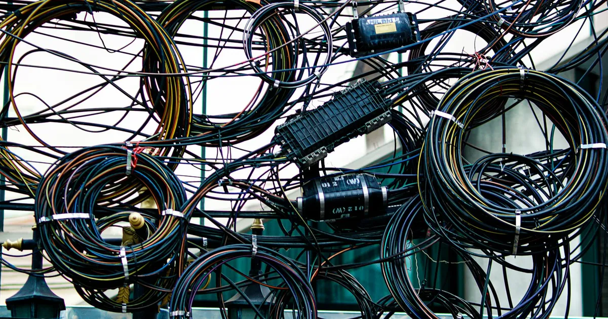 Intricate network of tangled power and communication cables outdoors.