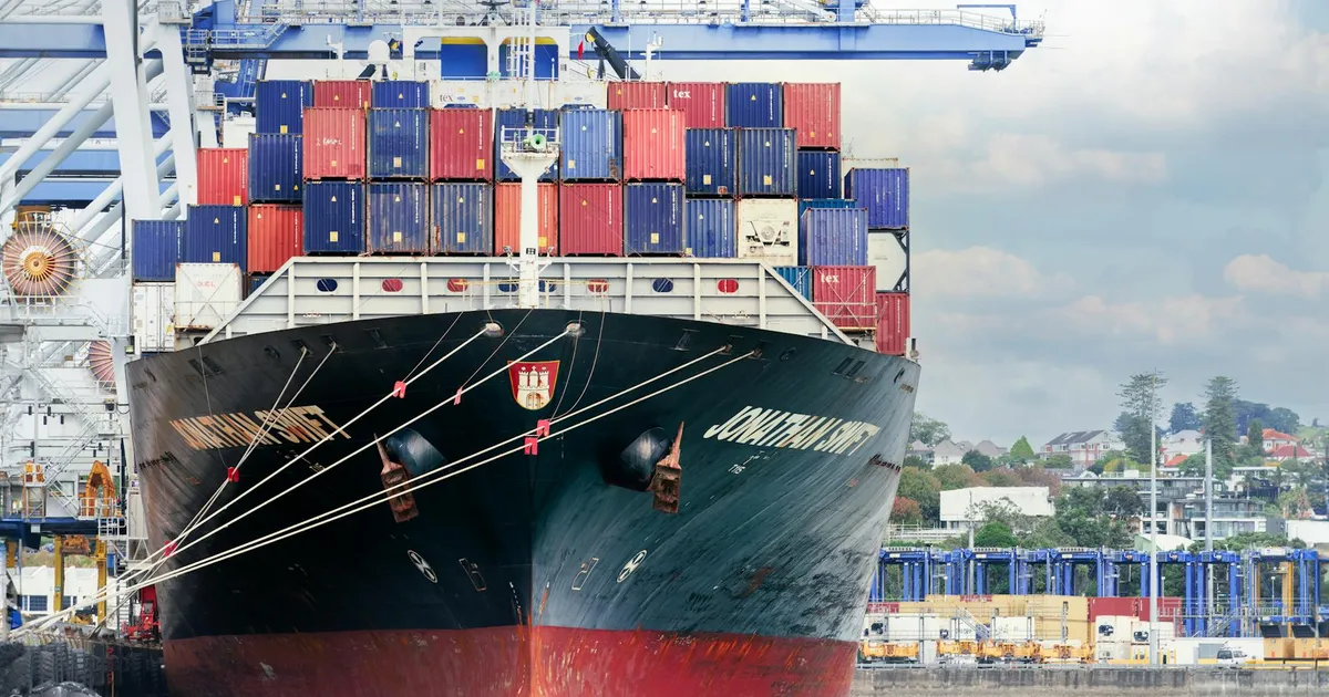 A large cargo ship with colorful containers docked at Auckland Port, New Zealand.