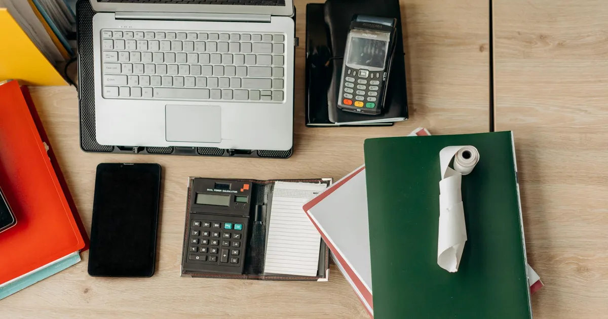 An organized office desk featuring a laptop, calculator, payment terminal, and documents.